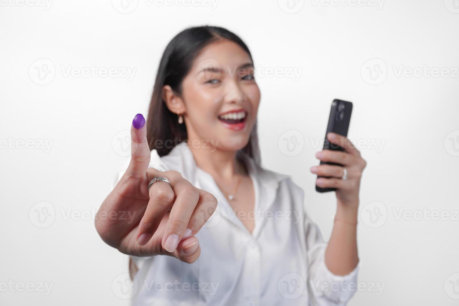 vrolijk Aziatisch vrouw trots tonen weinig vinger gedoopt in Purper inkt na stemmen voor president en parlement verkiezing terwijl links hand- Holding telefoon, uitdrukken opwinding en geluk foto