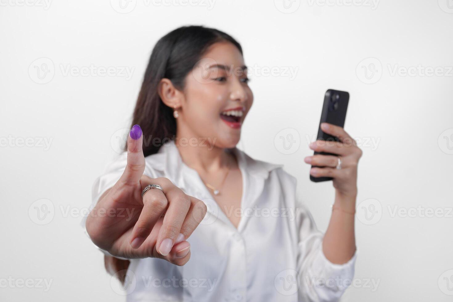 vrolijk Aziatisch vrouw trots tonen weinig vinger gedoopt in Purper inkt na stemmen voor president en parlement verkiezing terwijl links hand- Holding telefoon, uitdrukken opwinding en geluk foto