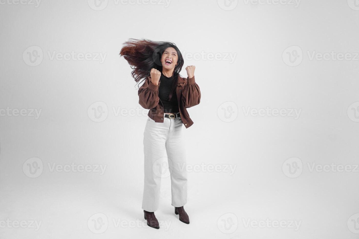 actief Aziatisch meisje is jumping en verhogen handen omhoog slijtage bruin jasje, geïsoleerd wit kleur achtergrond foto