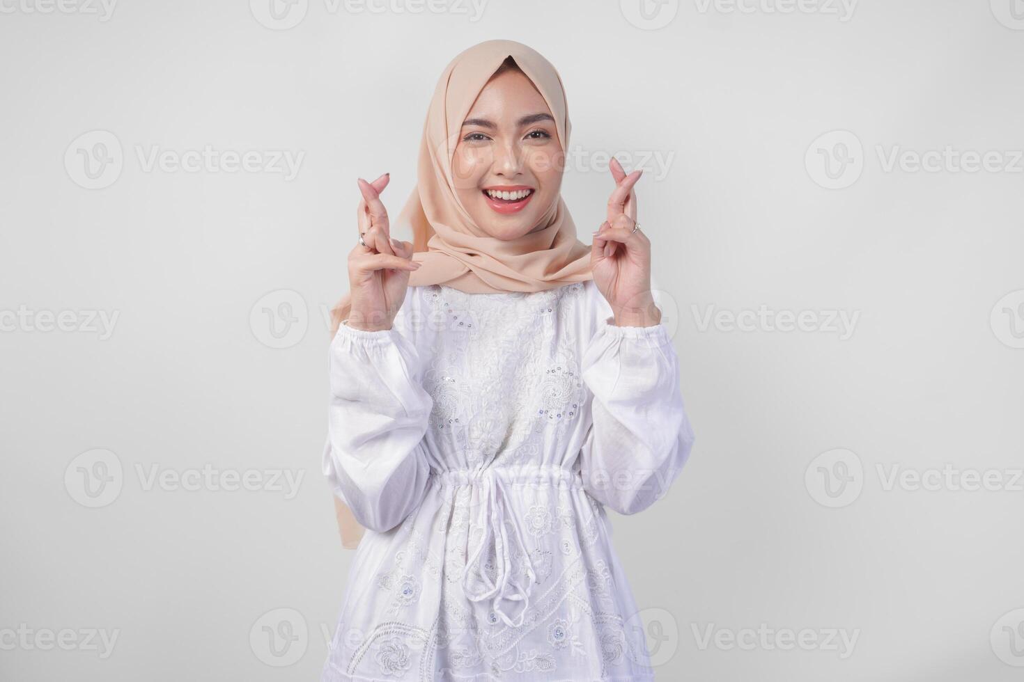 mooi Aziatisch vrouw vervelend hijab en wit jurk met vingers poseren een wens me geluk gebaar, staand over- geïsoleerd wit achtergrond. Ramadan en eid mubarak concept foto