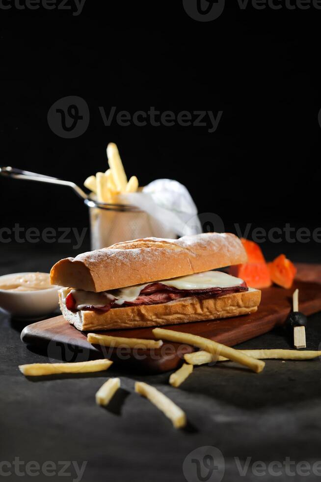 geroosterd rundvlees sub belegd broodje met Frans Patat emmer geserveerd Aan houten bord geïsoleerd Aan donker achtergrond kant visie van ontbijt voedsel foto