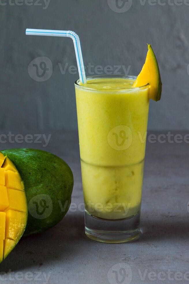 gezond mango sap vers sap geserveerd in glas met mango plak en rietje kant visie Aan grijs achtergrond foto