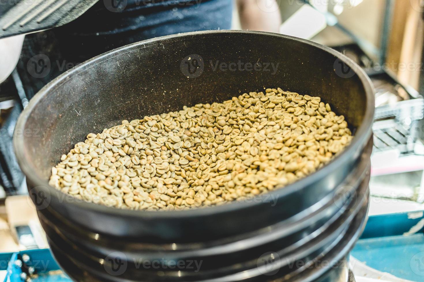 gewaswerker die rauwe koffiebonen in de koffiebrander giet foto