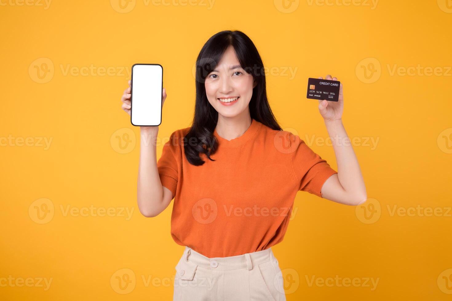 blij Aziatisch vrouw in haar jaren '30, presentatie van smartphone en credit kaart Aan geel achtergrond. beveiligen online betaling boodschappen doen foto