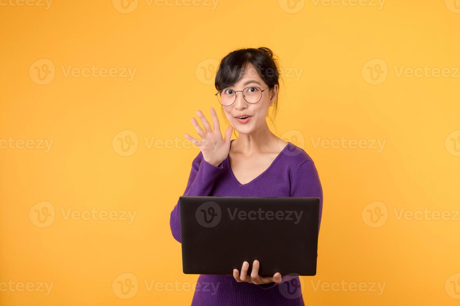 een portret van een jong en zelfverzekerd zakenvrouw vervelend een Purper overhemd en bril, Holding een laptop, betekenend haar expertise en kennis in de digitaal wereld tegen een geel achtergrond. foto