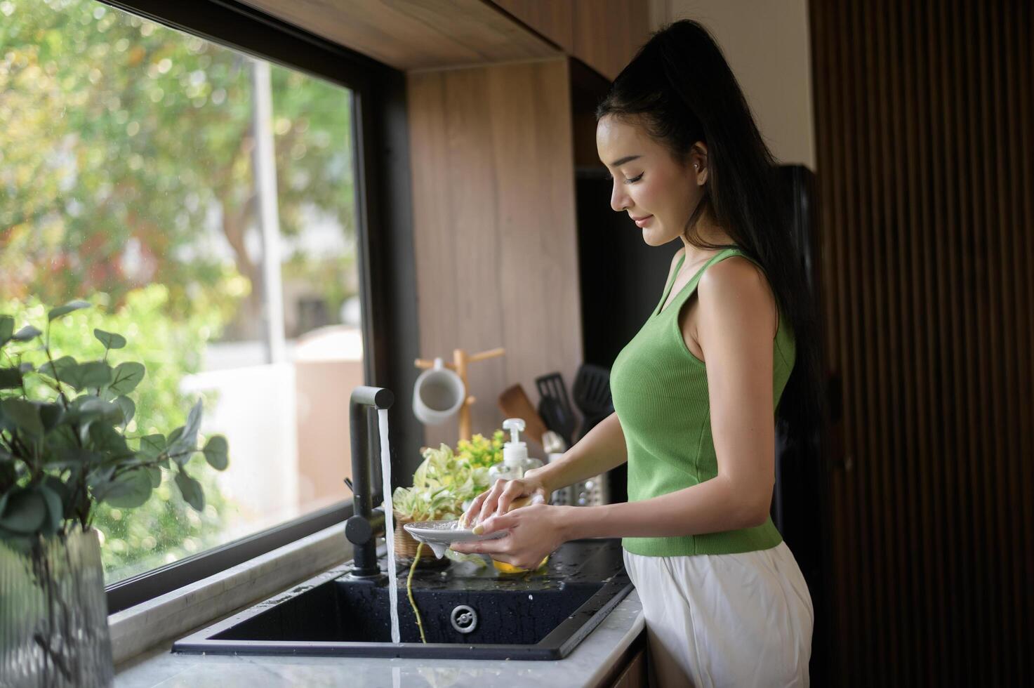 Aziatisch vrouw het wassen gerechten in de keuken wastafel Bij huis foto