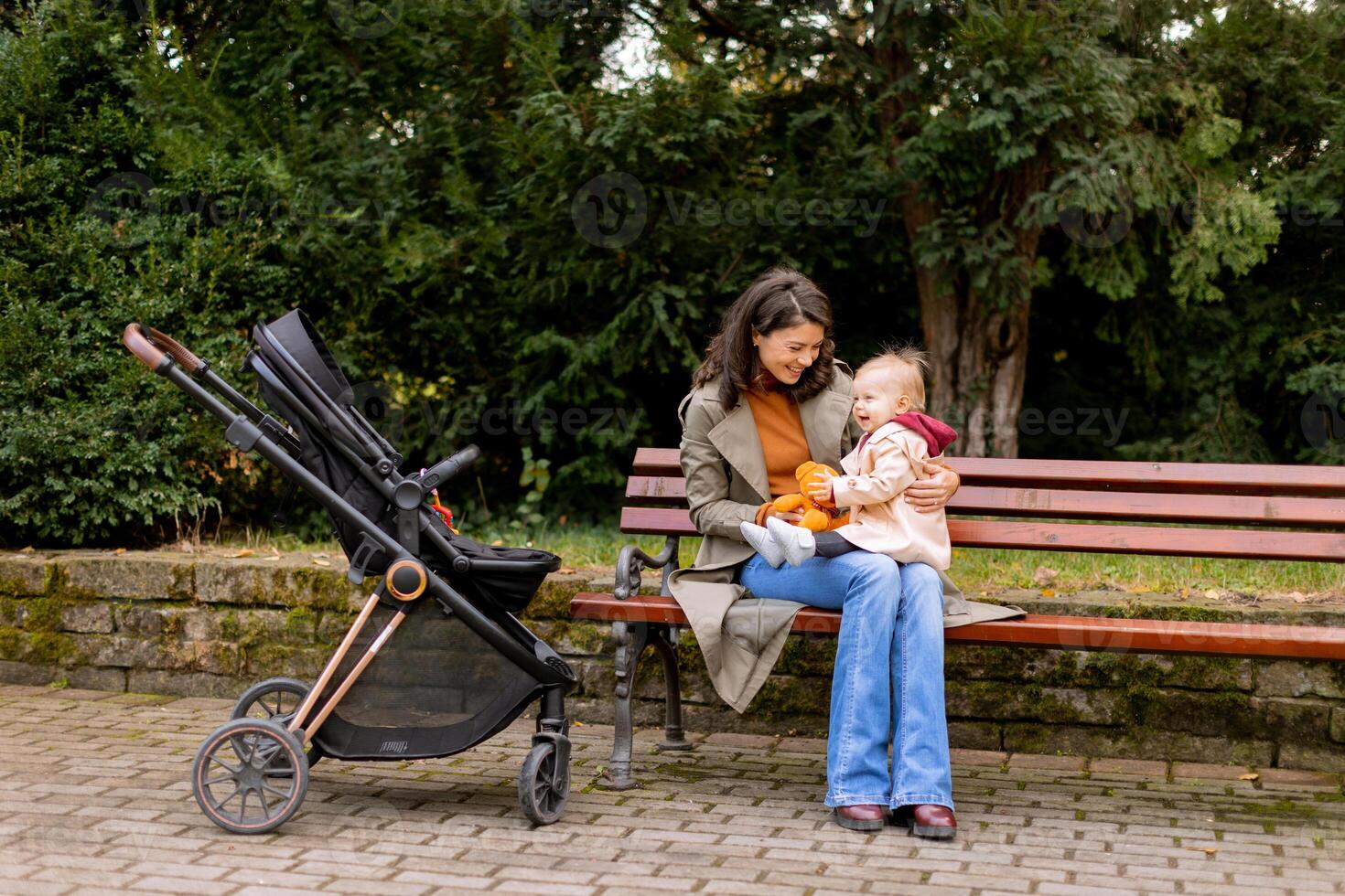 jong vrouw zittend Aan een bank met schattig baby meisje in de herfst park foto