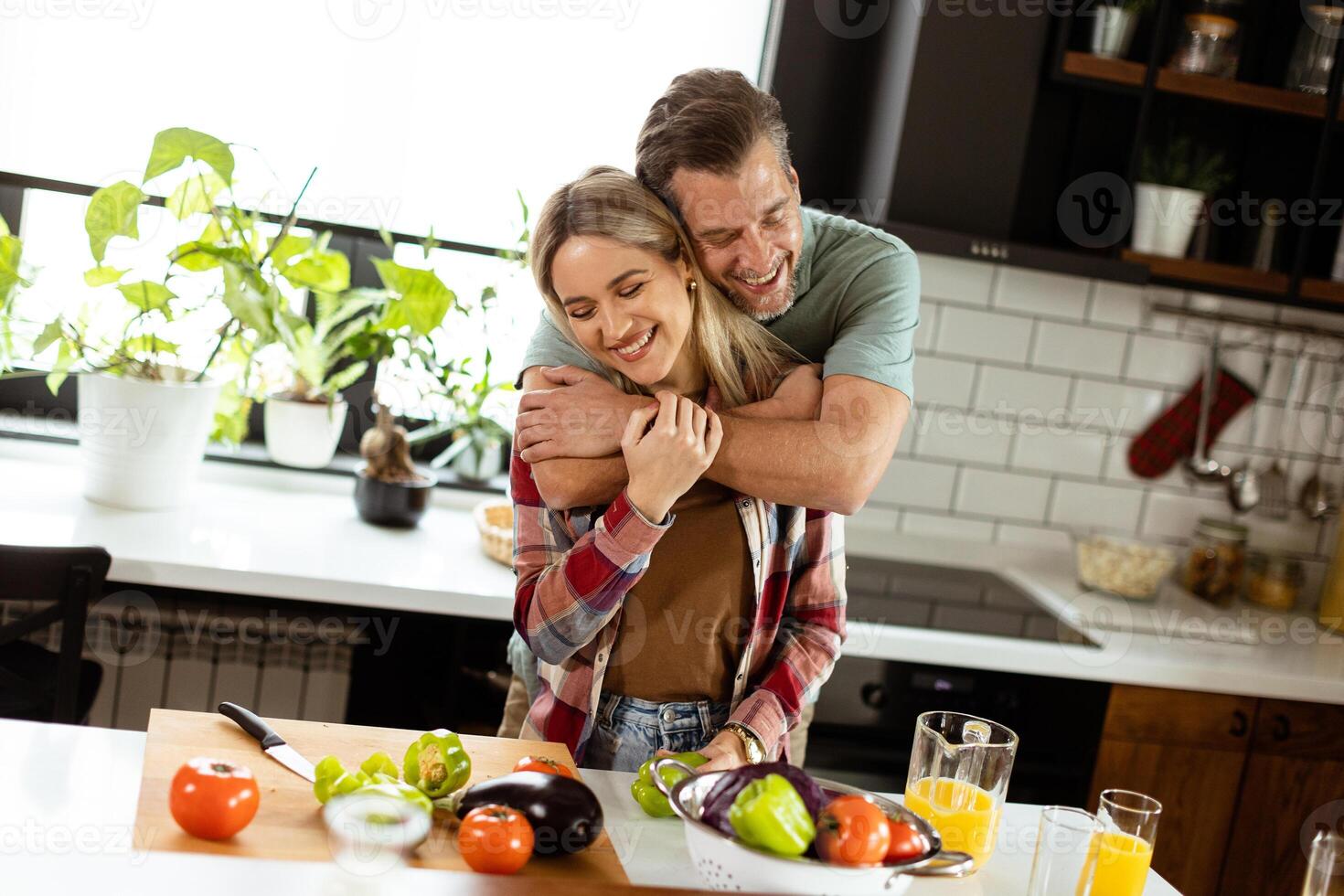 Mens en vrouw delen een warm knuffel in een knus keuken, omringd door Koken gereedschap en een pot sudderen Aan de fornuis foto