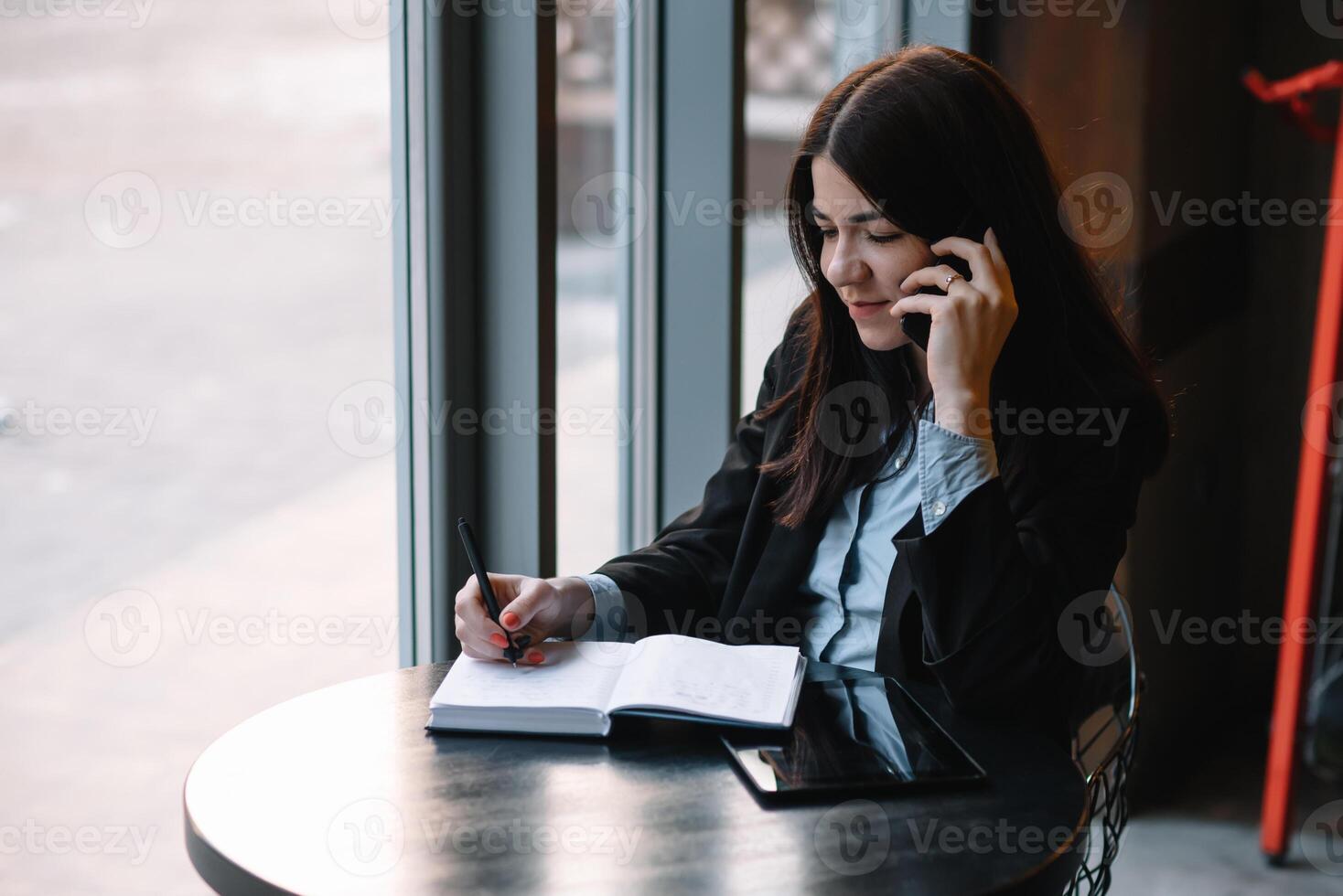 zakenvrouw pratend Aan de telefoon en nemen aantekeningen foto