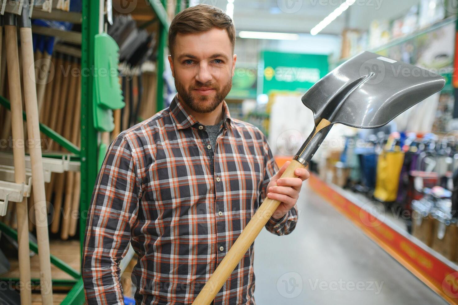 portret van een gelukkig jong Mens en klant buying een Schep terwijl boodschappen doen Bij de hardware op te slaan foto