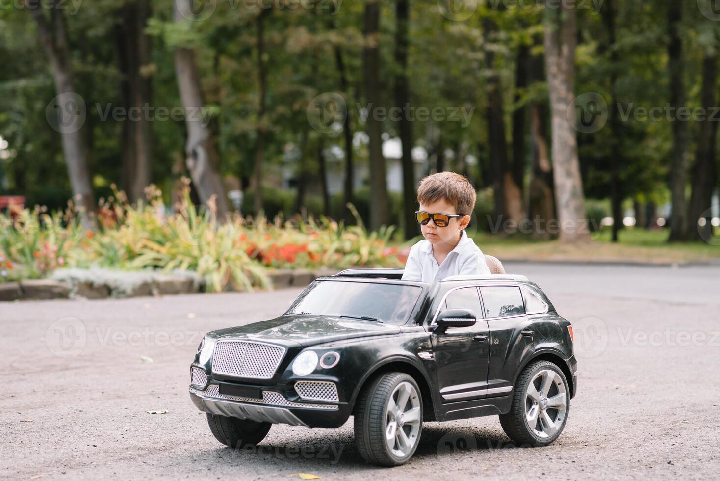 schattig jongen in rijden een zwart elektrisch auto in de park. grappig jongen ritten Aan een speelgoed- elektrisch auto. kopiëren ruimte. foto