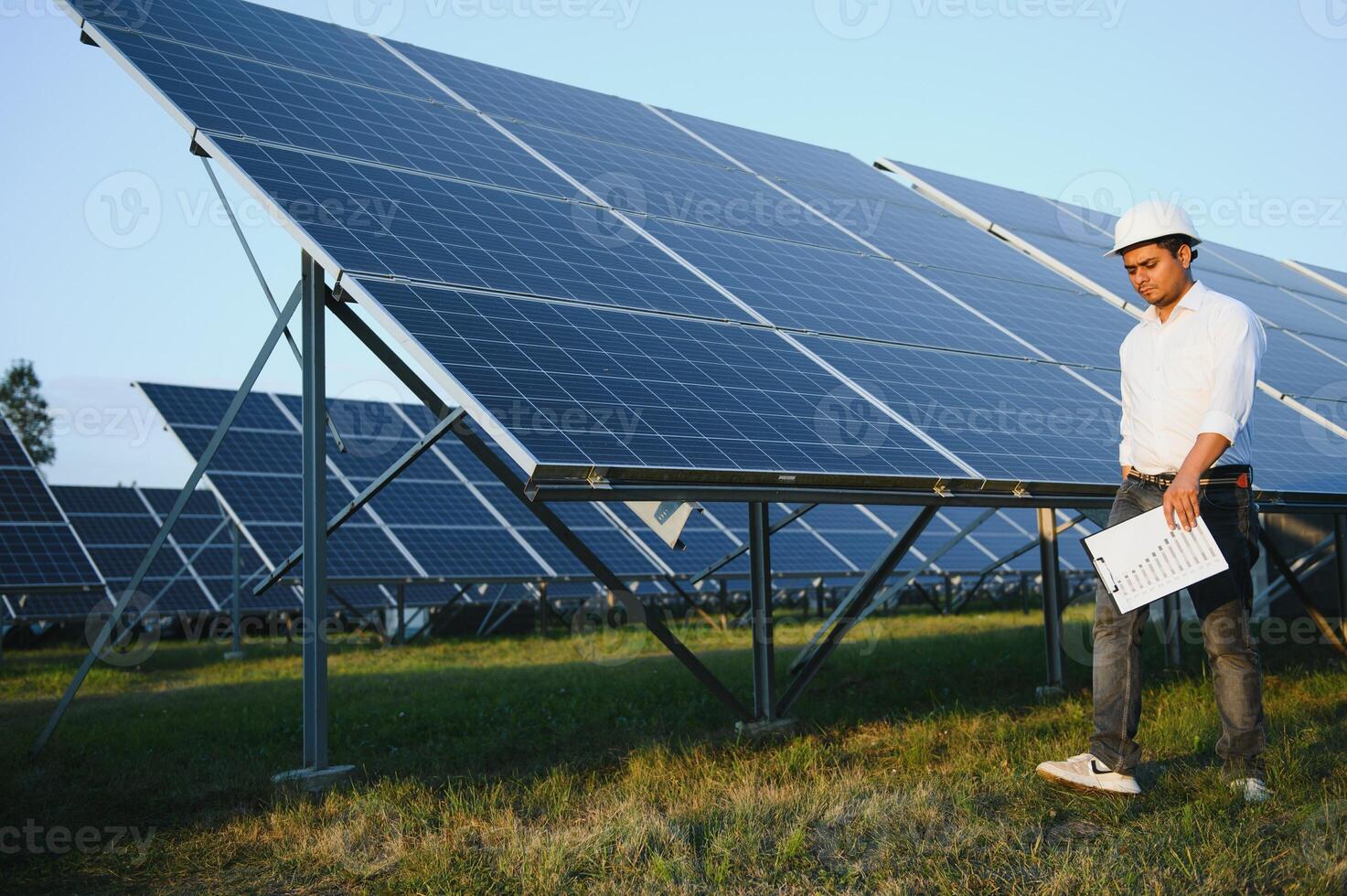 portret van jong Indisch mannetje ingenieur staand in de buurt zonne- panelen, met Doorzichtig blauw lucht achtergrond, hernieuwbaar en schoon energie. vaardigheid Indië, kopiëren ruimte foto