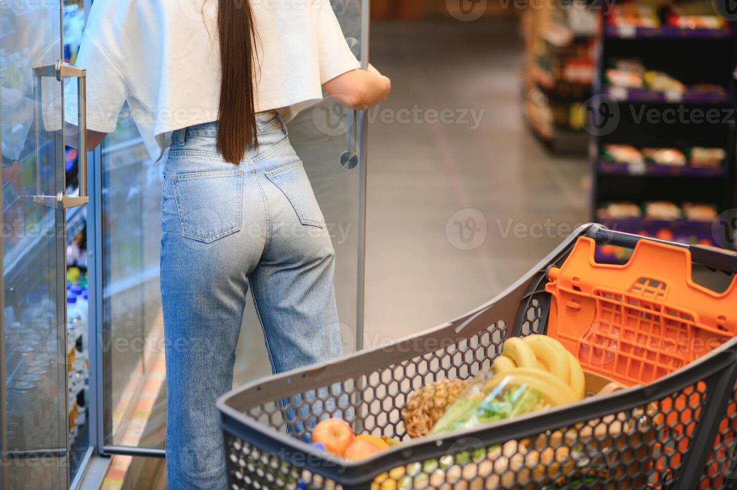 jong tevreden pret vrouw in gewoontjes kleren boodschappen doen Bij supermarkt op te slaan met kruidenier kar foto