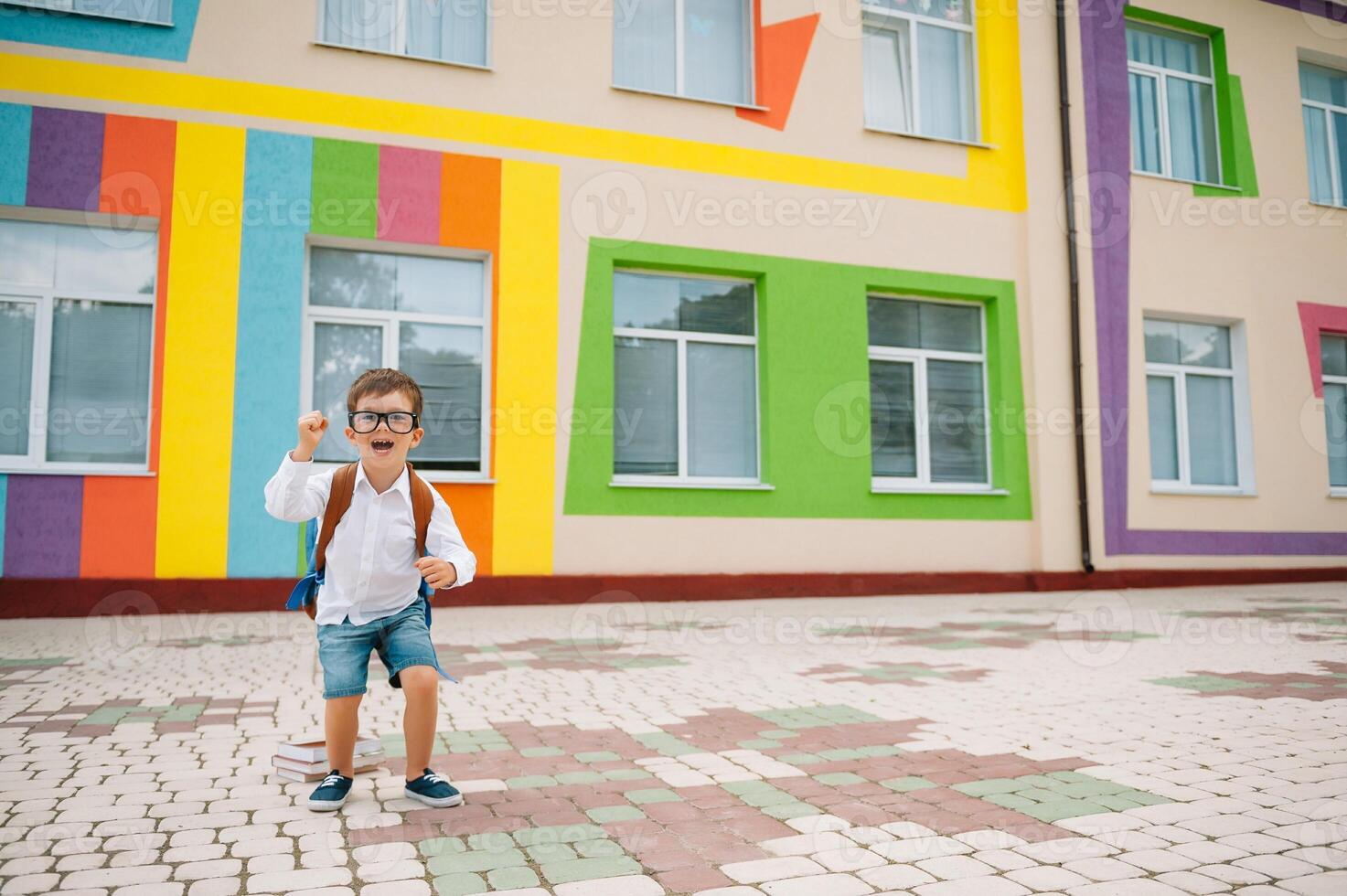 terug naar school. gelukkig glimlachen jongen in bril is gaan naar school- voor de eerste tijd. kind met rugzak en boek buitenshuis. begin van lessen. eerste dag van vallen foto