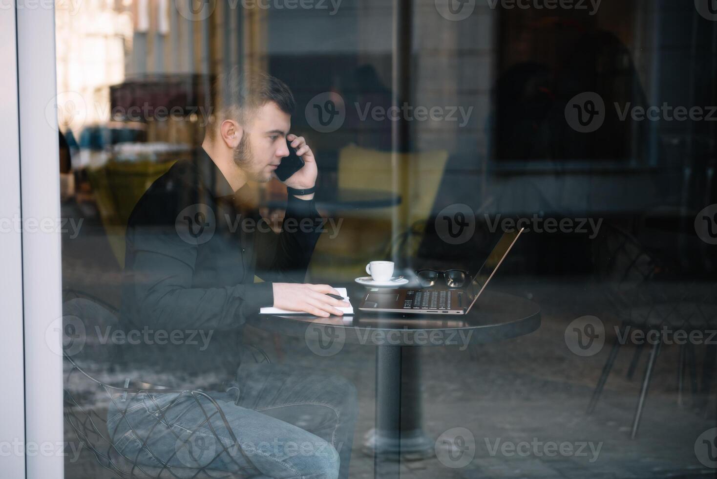 jong zakenman pratend Aan mobiel telefoon terwijl werken Aan laptop in cafe. foto