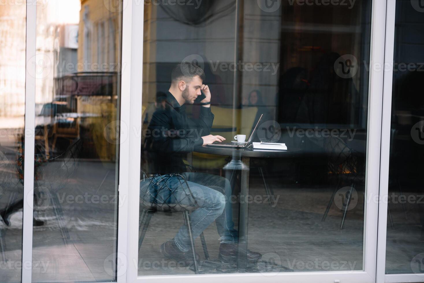 jong zakenman pratend Aan mobiel telefoon terwijl werken Aan laptop in cafe. foto