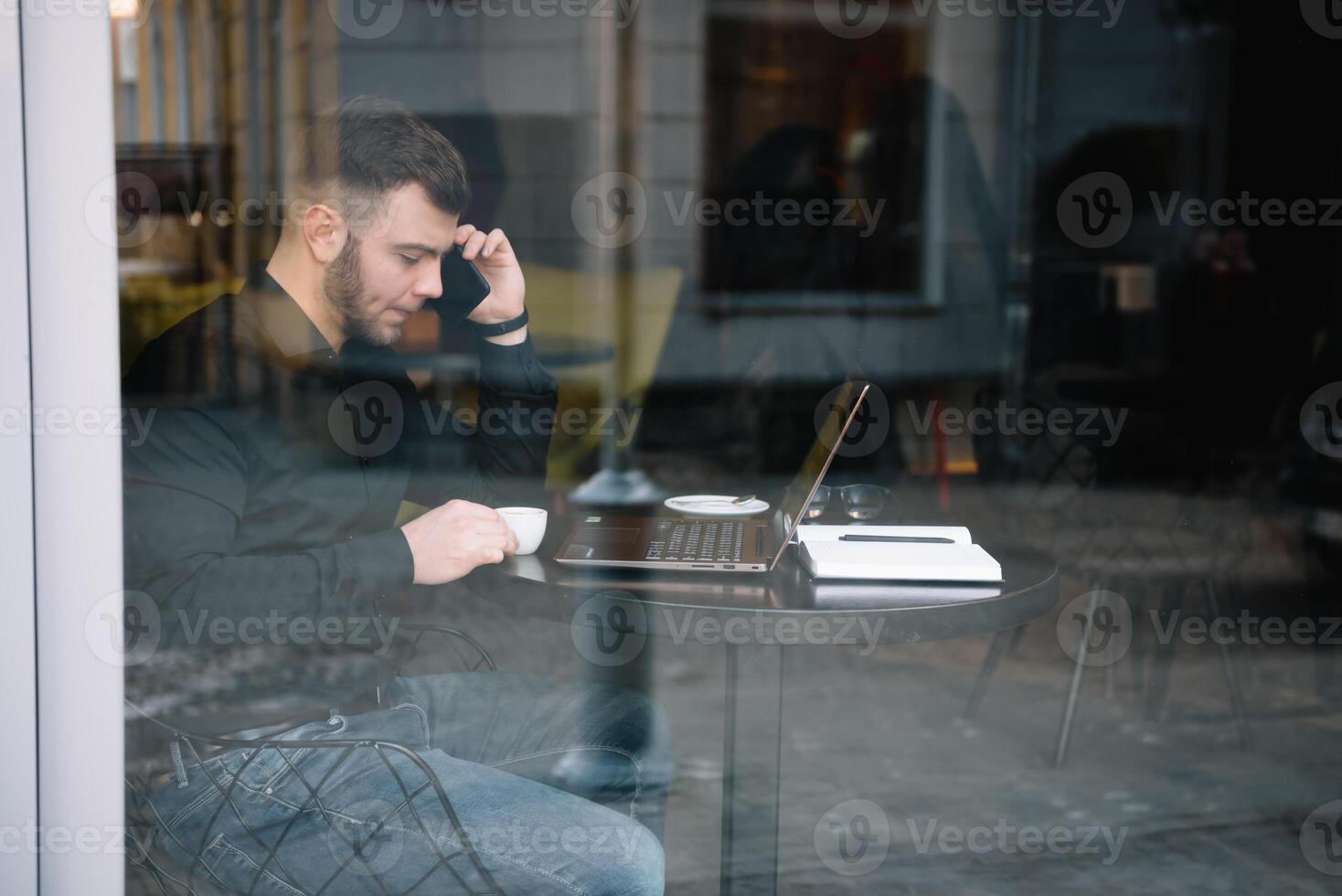 jong zakenman pratend Aan mobiel telefoon terwijl werken Aan laptop in cafe. foto