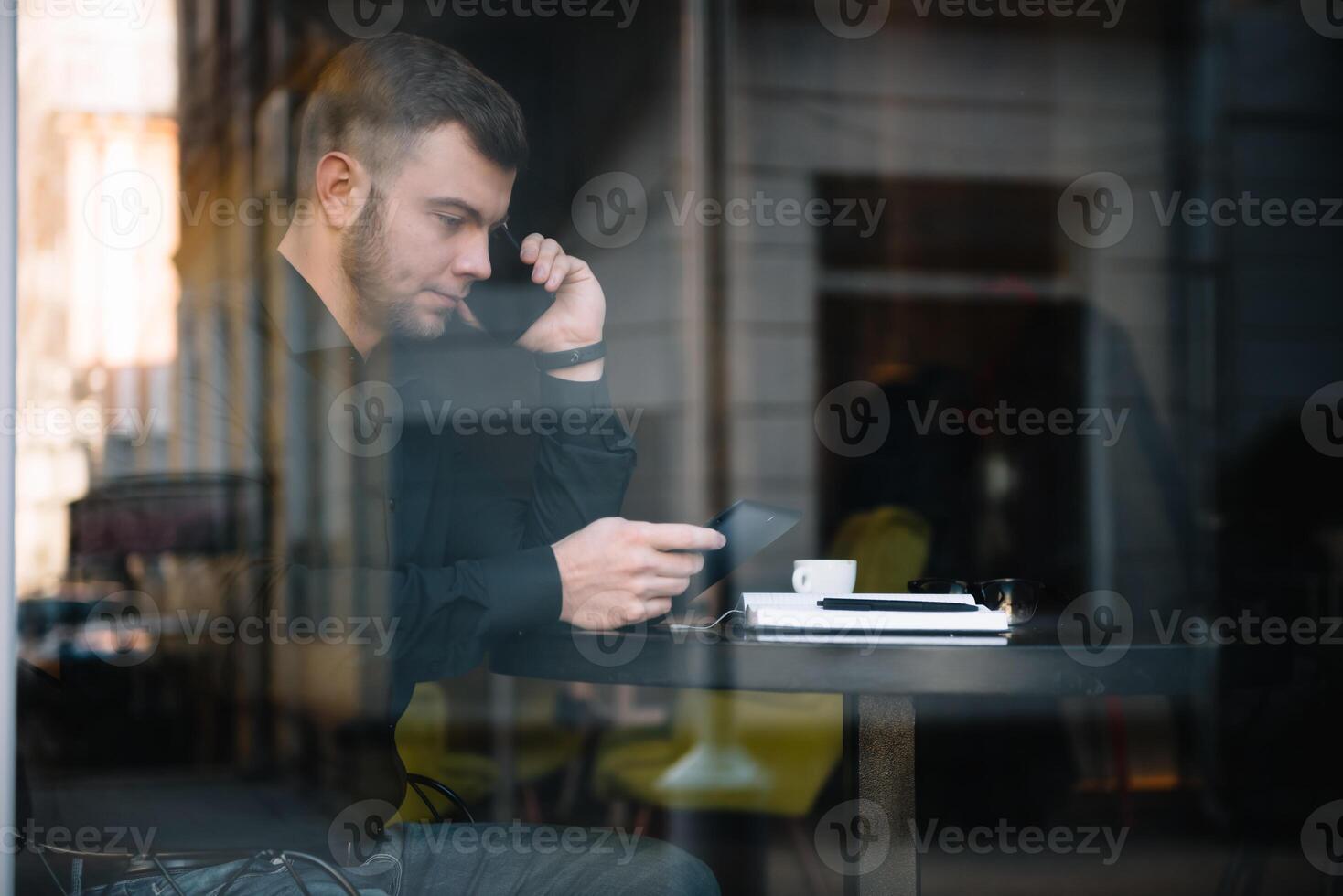 jong zakenman pratend Aan mobiel telefoon terwijl werken Aan laptop in cafe. foto