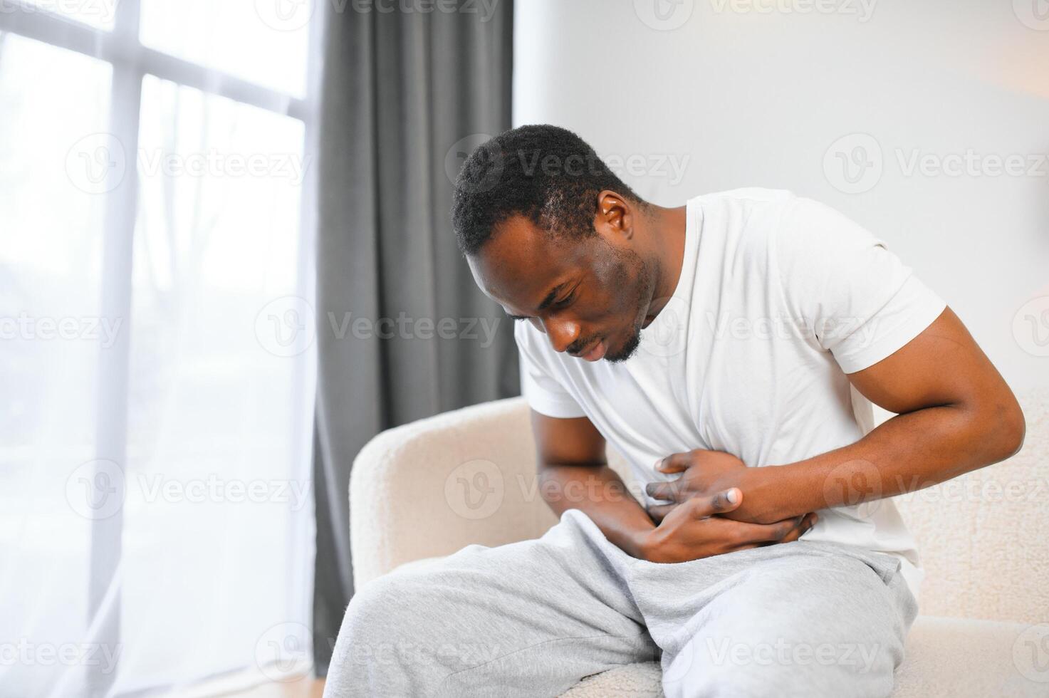 Afrikaanse Amerikaans vent hebben maag pijn na aan het eten aanraken pijn doen maag lijden van pijn zittend Aan sofa Bij huis. foto