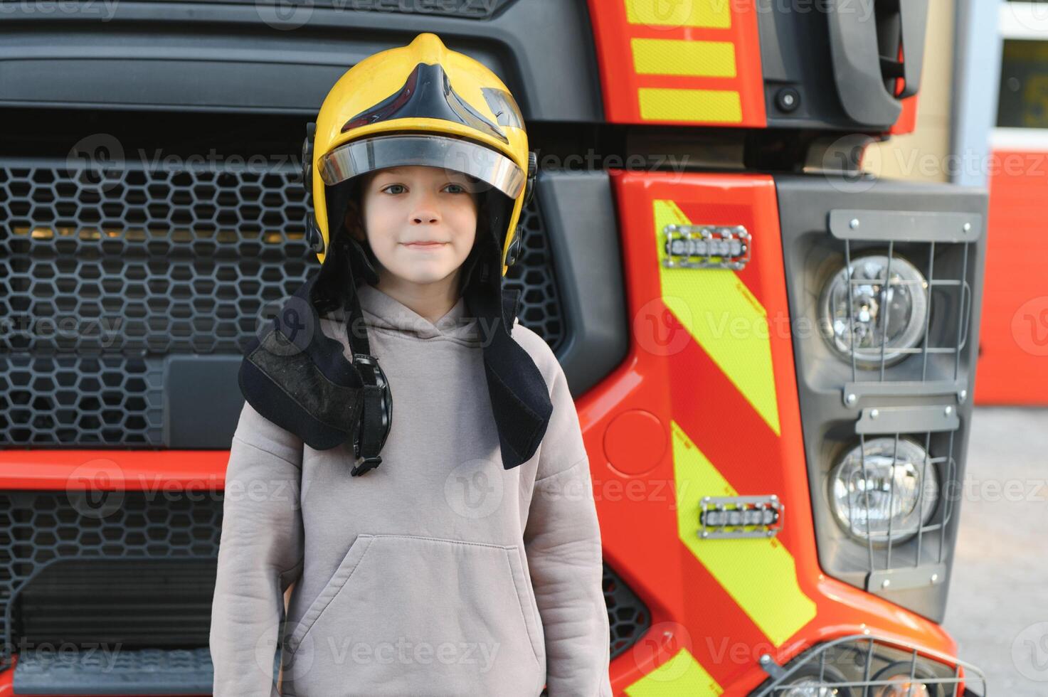 een jongen vervelend een brandweerman helm in de buurt een brand vrachtwagen. foto