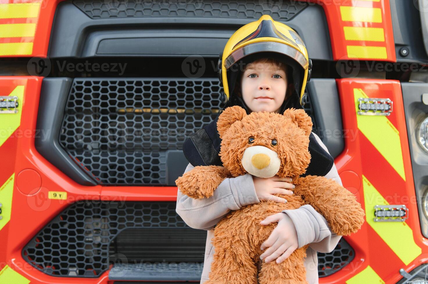 een jongen vervelend een brandweerman helm in de buurt een brand vrachtwagen. foto