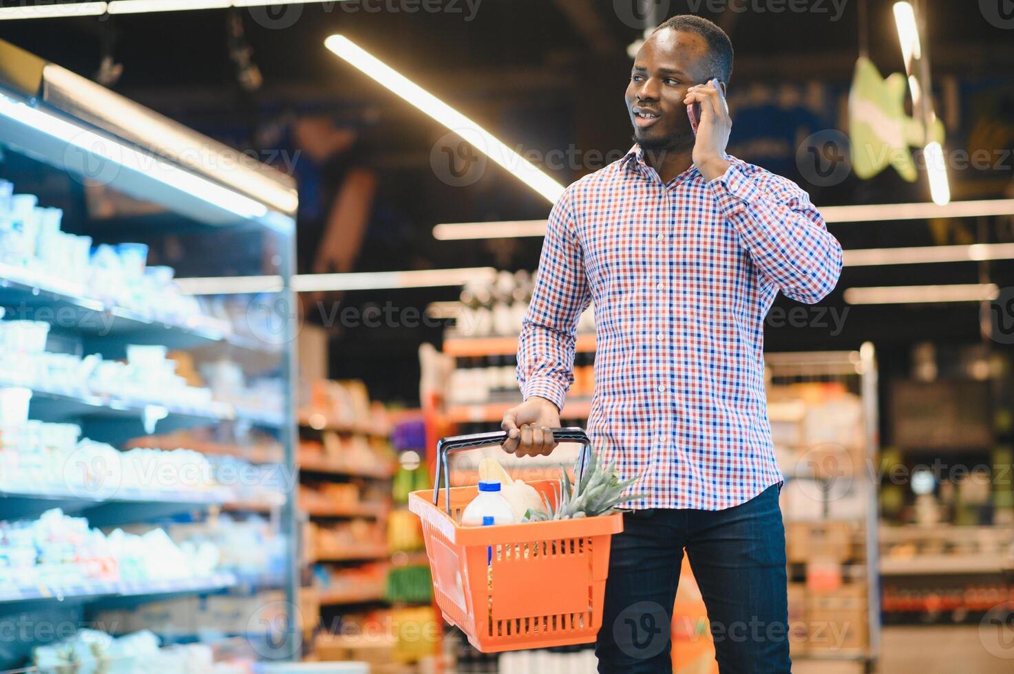 Afrikaanse Amerikaans Mens pratend Aan mobiele telefoon chatten terwijl boodschappen doen boodschappen in supermarkt foto