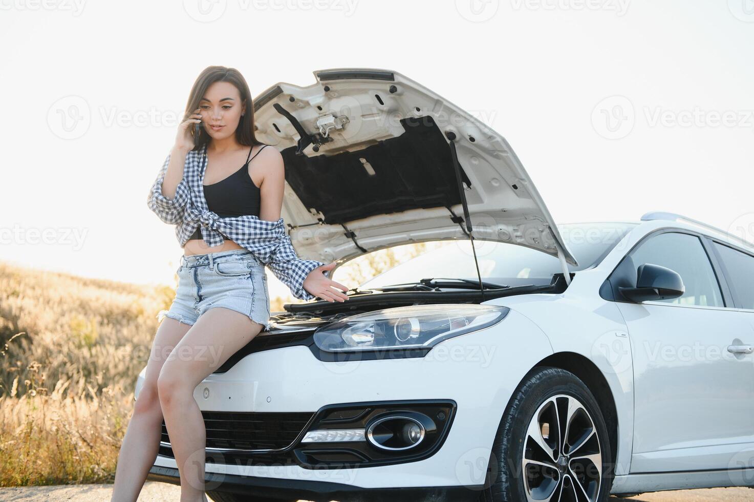 Dames pratend Aan de telefoon over probleem met haar auto ze kan niet. jong sexy meisje overlegt Aan de telefoon gedurende auto reparatie foto