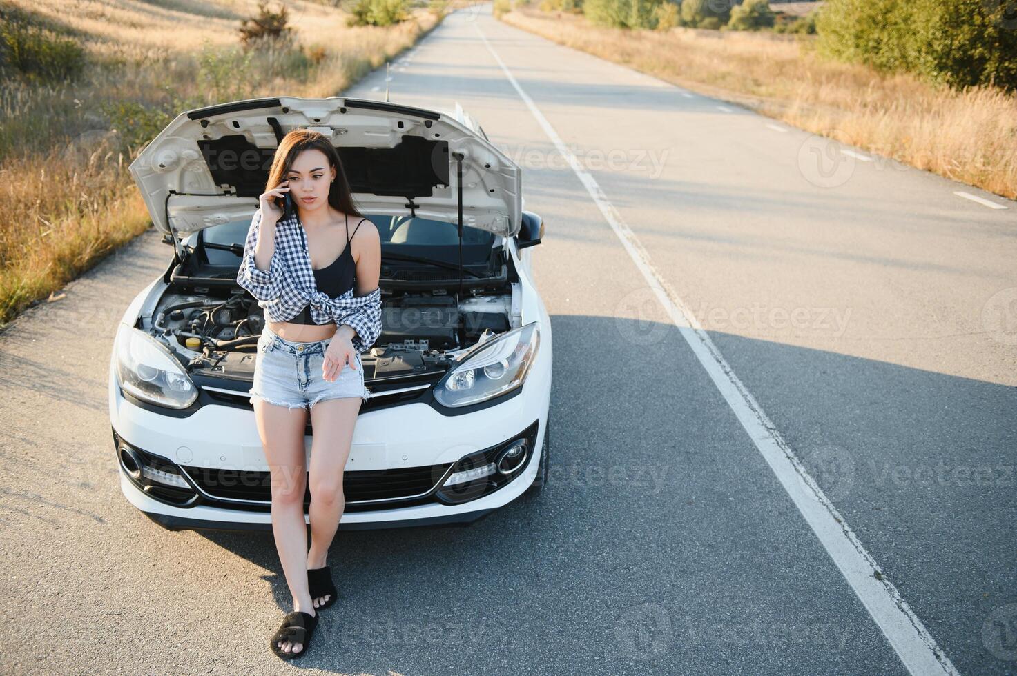 Dames pratend Aan de telefoon over probleem met haar auto ze kan niet. jong sexy meisje overlegt Aan de telefoon gedurende auto reparatie foto