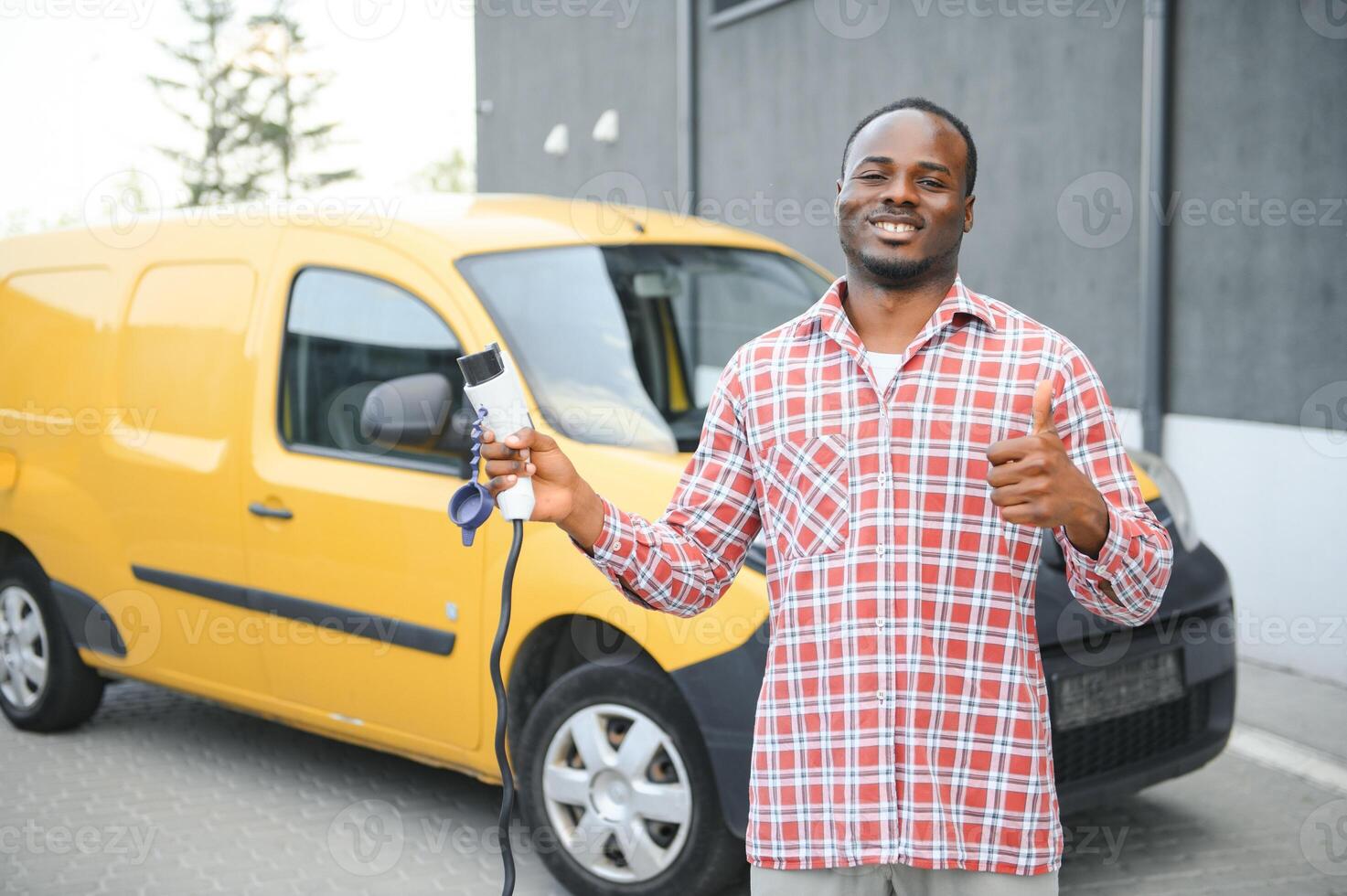 Afrikaanse Amerikaans Mens staat De volgende naar elektrisch levering bestelwagens Bij elektrisch voertuig opladen station foto