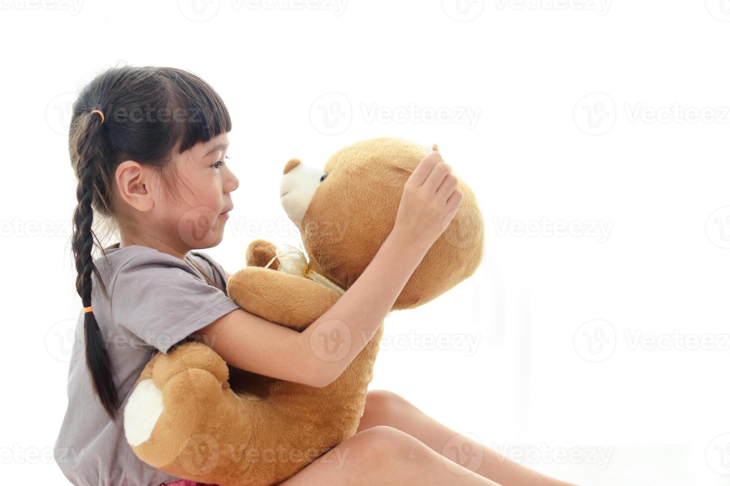 schattig weinig Aziatisch meisje hebben pret ze omhelsd een groot bruin teddy beer Aan de wit bed. concept van familie, vriendschap foto