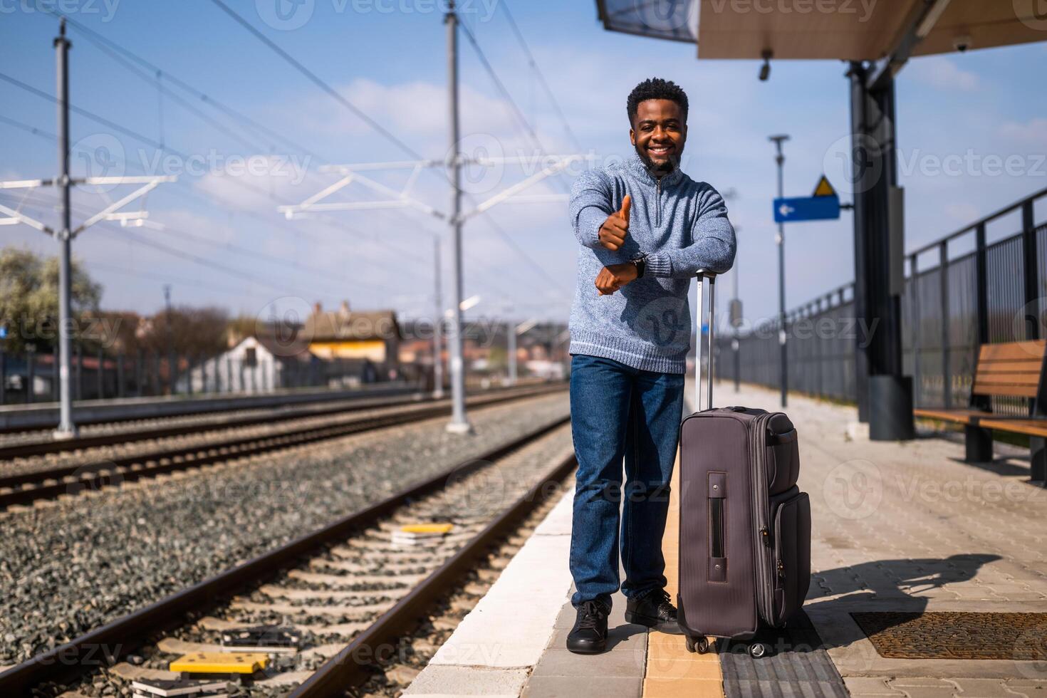 gelukkig Mens met koffer staand Aan spoorweg station en tonen duim omhoog. foto