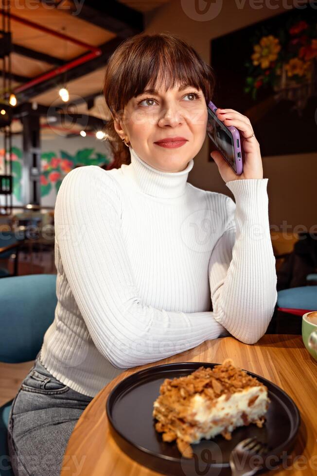 portret van glimlachen vrouw pratend Aan telefoon terwijl zittend in cafe, lunch breken foto