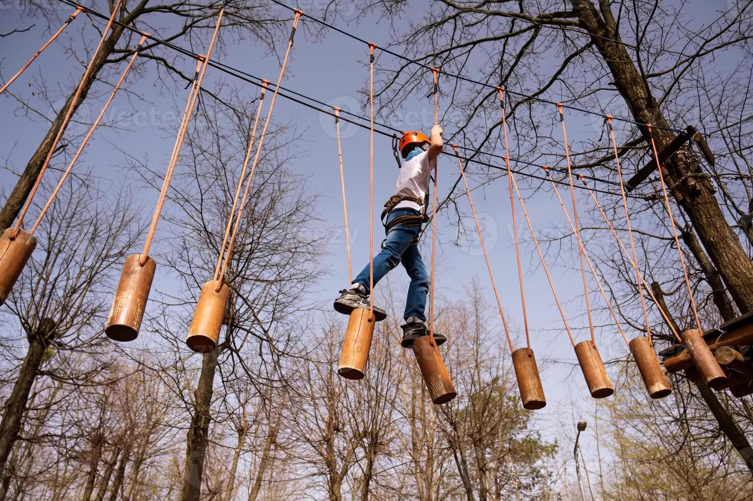 een jongen in een helm klimt een touw park in de voorjaar foto