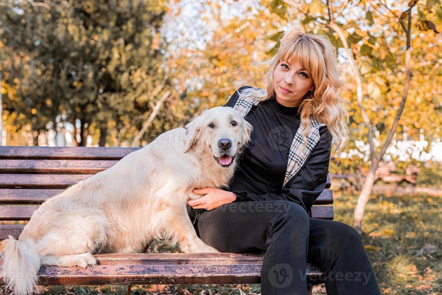 blonde blanke vrouw zit met haar gouden labrador retriever-hond op de bank in het park foto