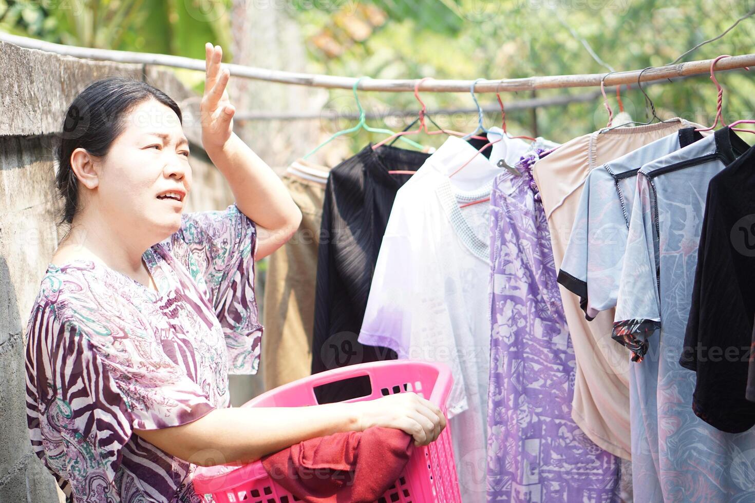 Aziatisch vrouw huisvrouw is werken , drogen kleding buitenshuis Aan zonnig dag. voelen heet. concept, werken of aan het doen buitenshuis werkzaamheid is risico naar warmte beroerte symptoom in heet weer conditie.globaal opwarming effect foto