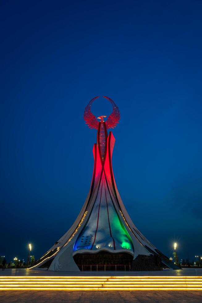 Oezbekistan, Tasjkent - mei 5, 2023 verlichte monument van onafhankelijkheid in de het formulier van een stele met een humo vogel, fonteinen en golvend vlaggen in de nieuw Oezbekistan park Bij nacht. foto