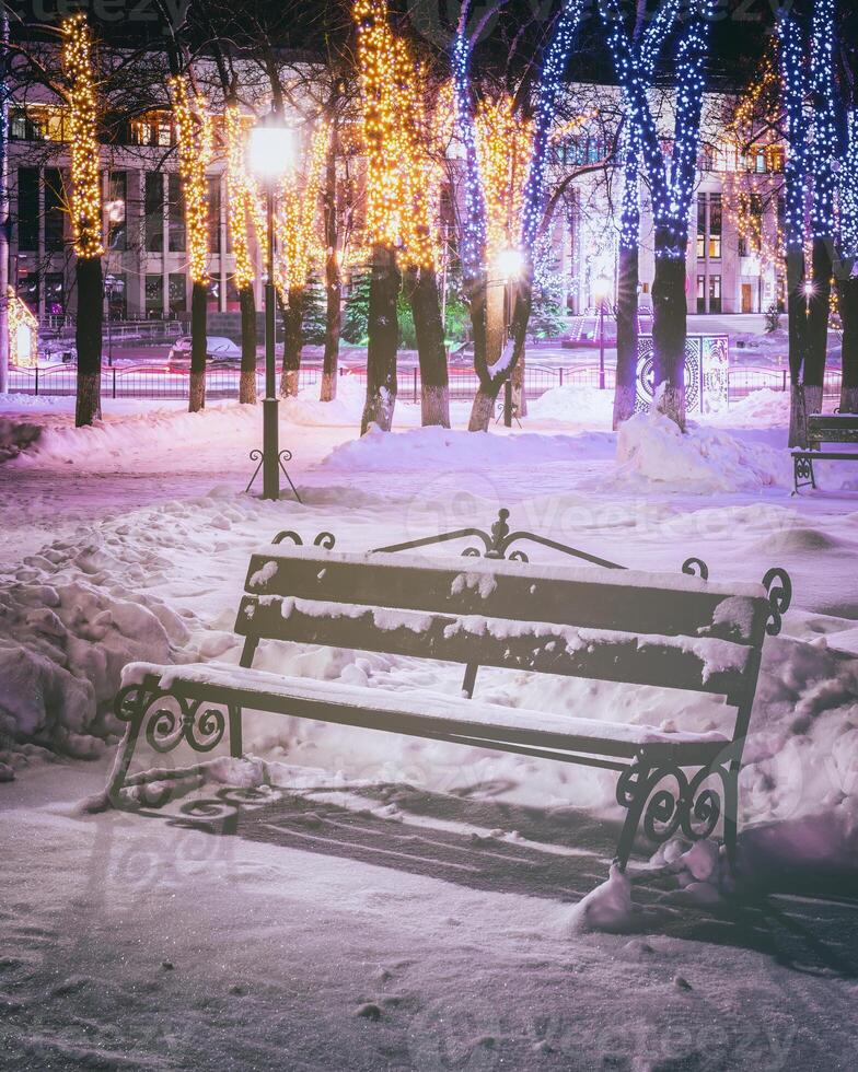 winter park Bij nacht met Kerstmis decoraties, gloeiend lantaarns, bestrating gedekt met sneeuw en bomen. wijnoogst film stijlvol. foto