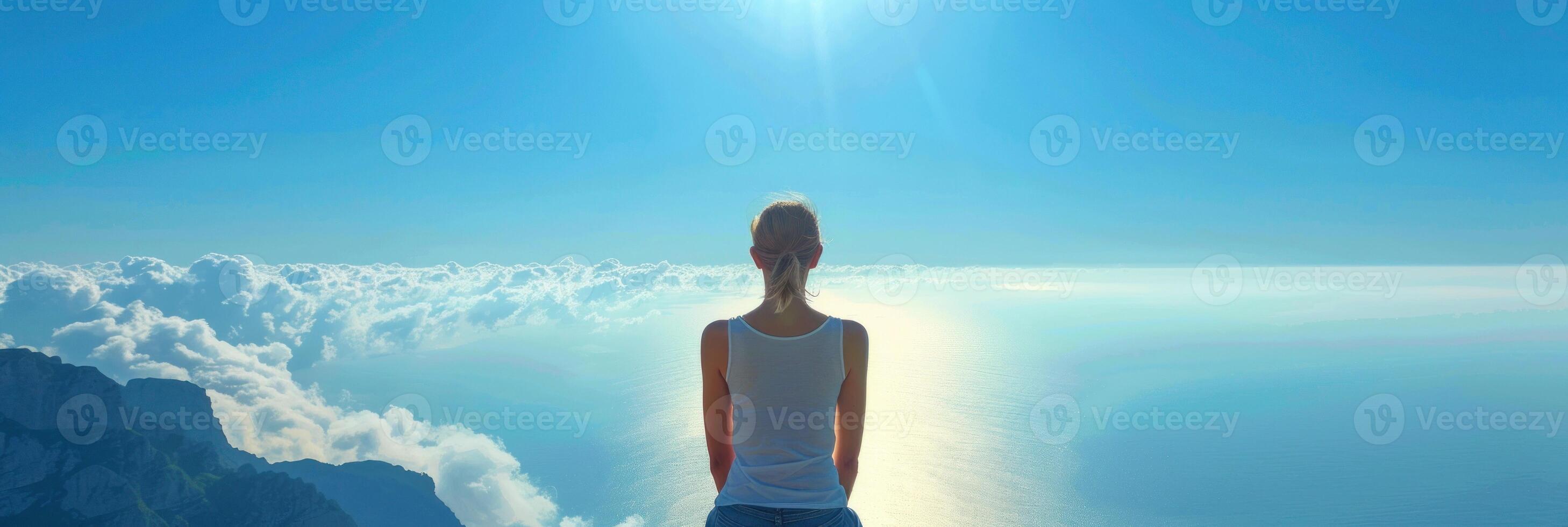 een vrouw staat Aan een berg piek, op zoek uit over- een zee van wolken hieronder foto