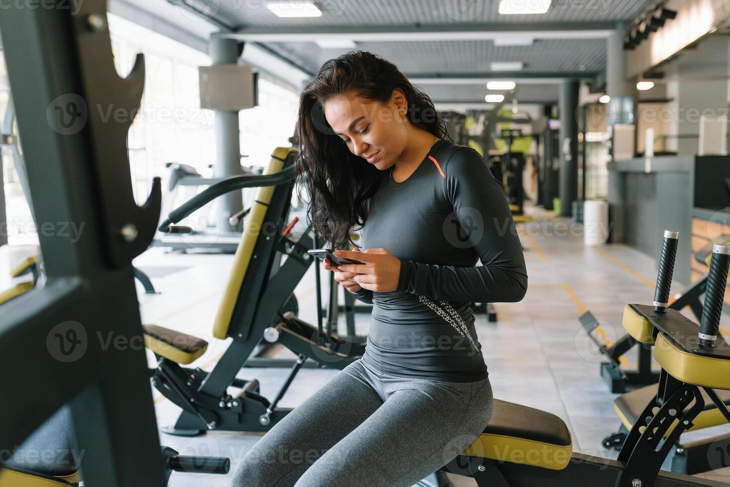 prachtig jong vrouw sms'en en sociaal netwerken terwijl in een Sportschool. foto