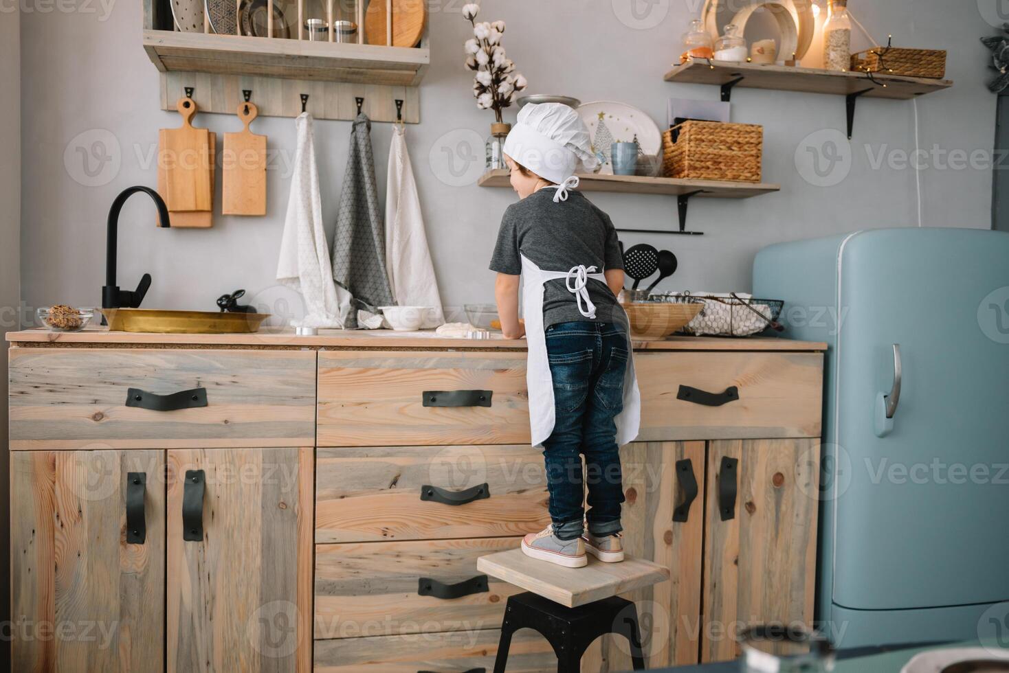 jong gelukkig mam en haar baby koken koekjes Bij huis in de keuken. Kerstmis eigengemaakt ontbijtkoek. schattig jongen met moeder in wit uniform en hoed gekookt chocola koekjes. foto