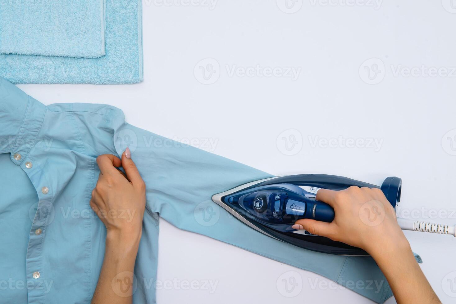 vrouw hand- strijken kleren top visie geïsoleerd Aan wit achtergrond. jong vrouw met ijzer strijken man's overhemd gezien van bovenstaand gedurende huiswerk. blauw ijzer Aan wit tafel foto