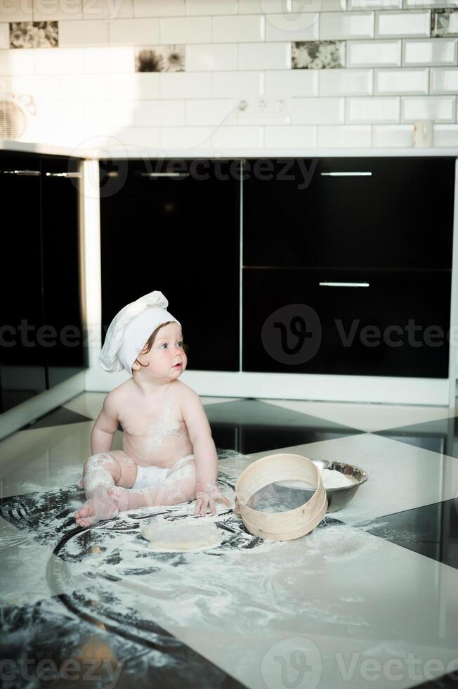 weinig jongen zittend Aan tapijt in keuken spelen met Koken potten. schattig jongen Koken in keuken Bij huis foto