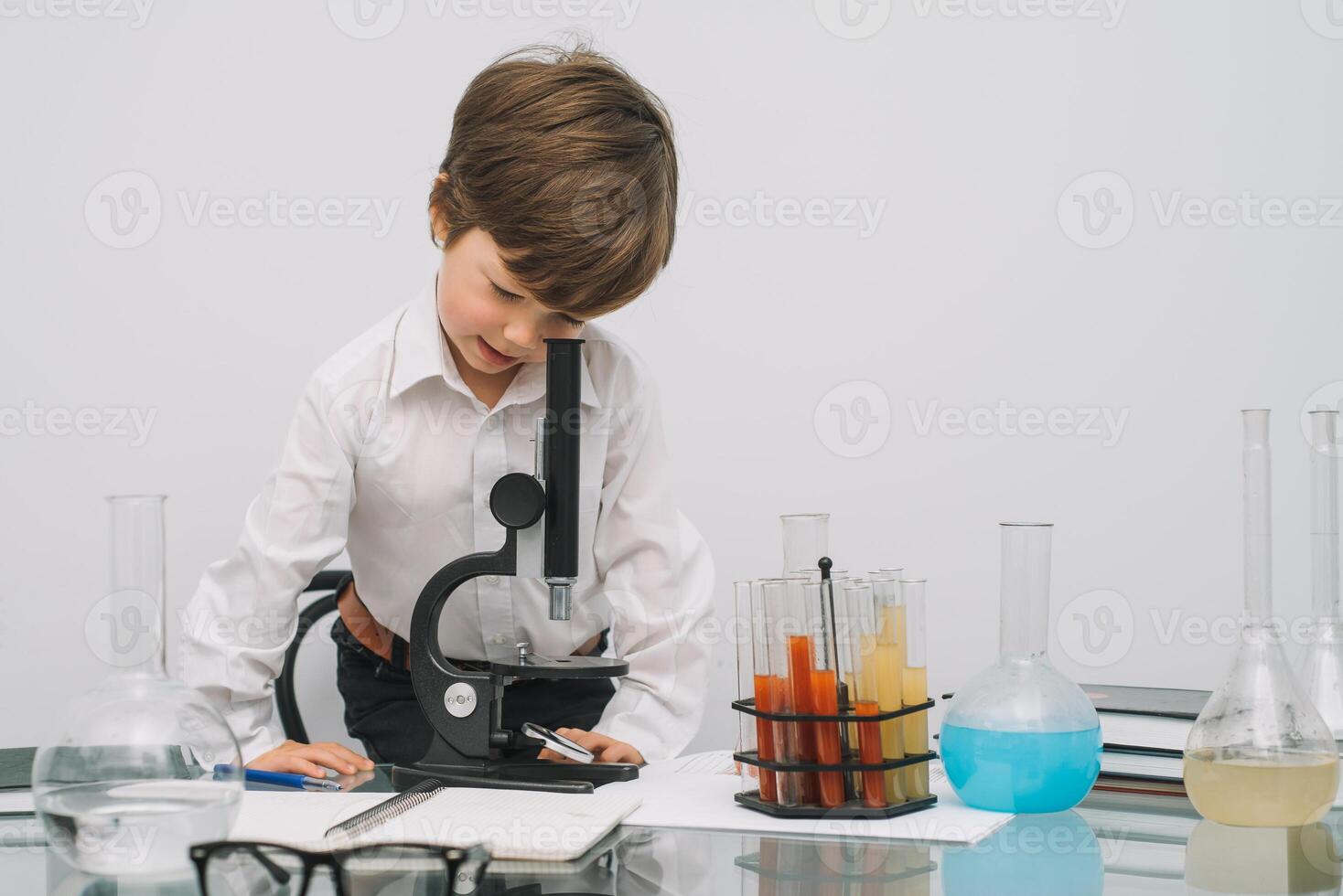 de jongen met een microscoop en divers kleurrijk kolven Aan een wit achtergrond. een jongen aan het doen experimenten in de laboratorium. explosie in de laboratorium. wetenschap en onderwijs foto