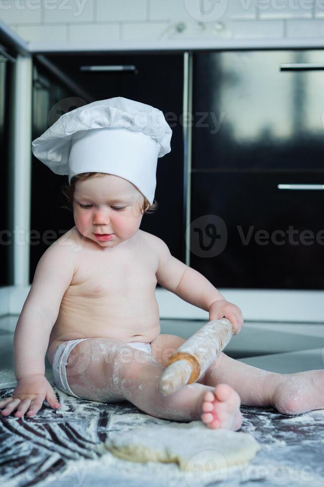 weinig jongen zittend Aan tapijt in keuken spelen met Koken potten. schattig jongen Koken in keuken Bij huis foto