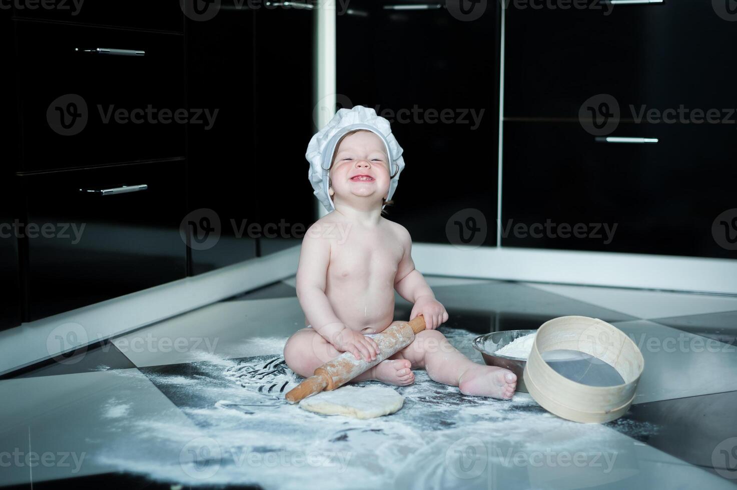 weinig jongen zittend Aan tapijt in keuken spelen met Koken potten. schattig jongen Koken in keuken Bij huis foto