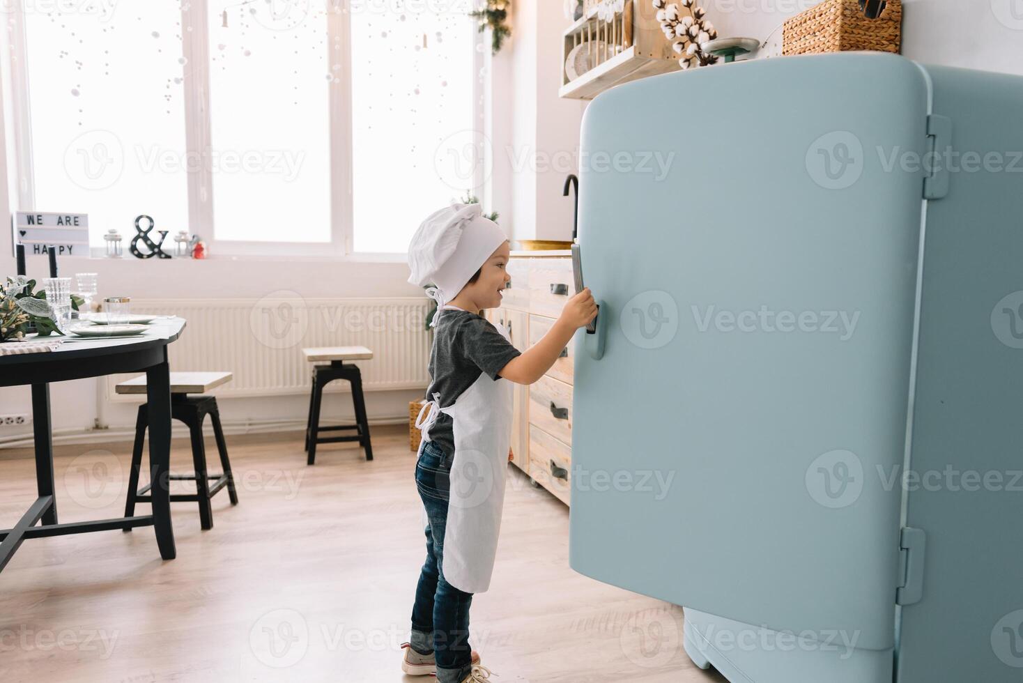 jong jongen schattig Aan de keuken koken chef in wit uniform en hoed in de buurt tafel. Kerstmis eigengemaakt ontbijtkoek. de jongen gekookt de chocola koekjes. foto