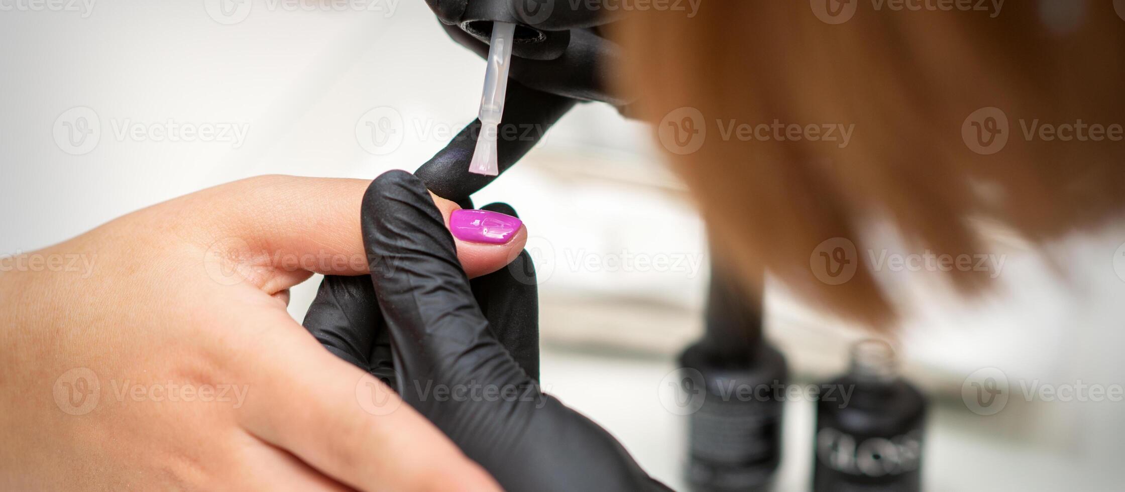 schilderij nagels van een vrouw. handen van manicure in zwart handschoenen toepassen roze nagel Pools Aan vrouw nagels in een schoonheid salon. foto