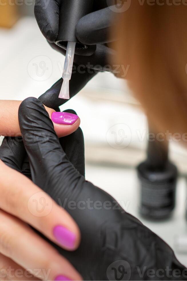 schilderij nagels van een vrouw. handen van manicure in zwart handschoenen toepassen roze nagel Pools Aan vrouw nagels in een schoonheid salon. foto