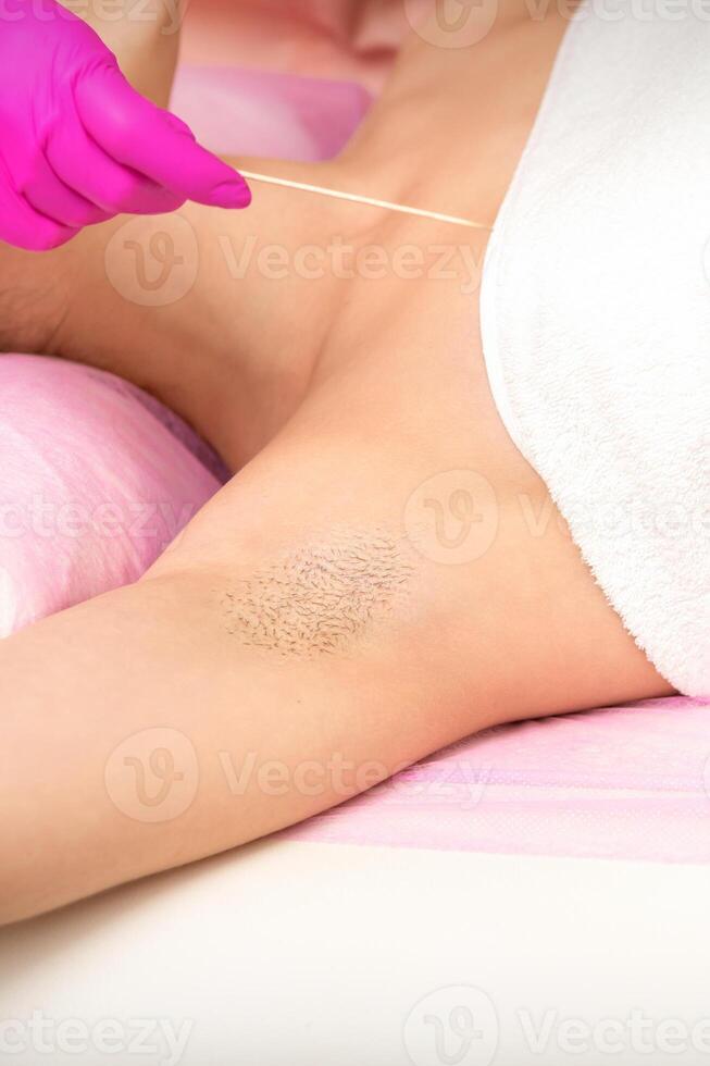 hand- in handschoen met spatel onthaart vrouw harig oksel in een spa. foto