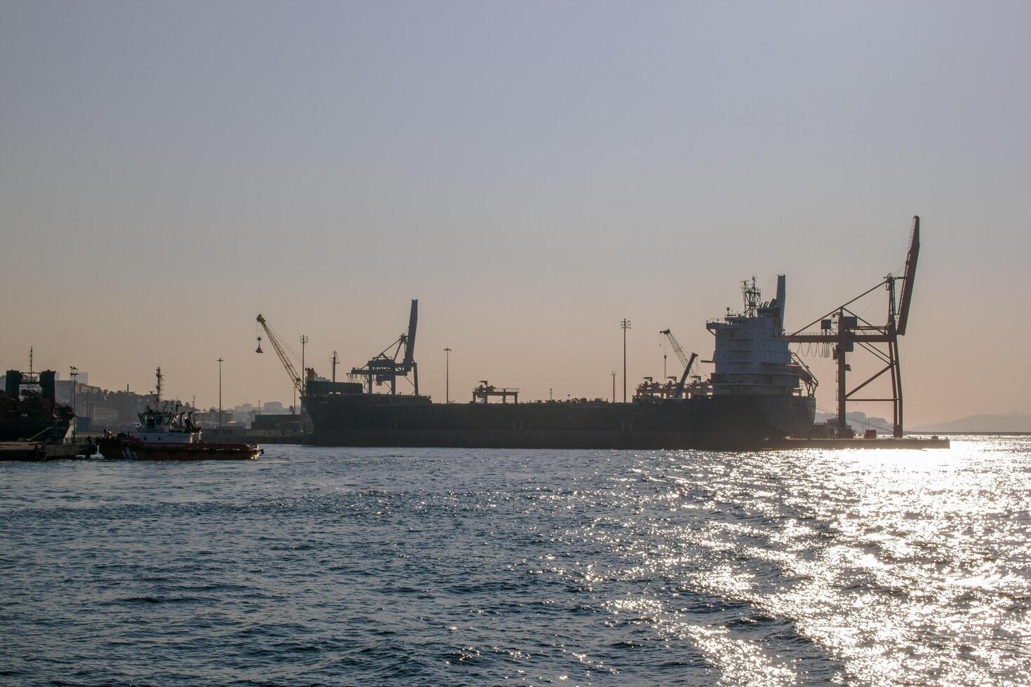 Istanbul, kalkoen - december 29, 2022. silhouet van een groot lading schip aangemeerd Bij zonsondergang met een sleepboot in de voorgrond. foto